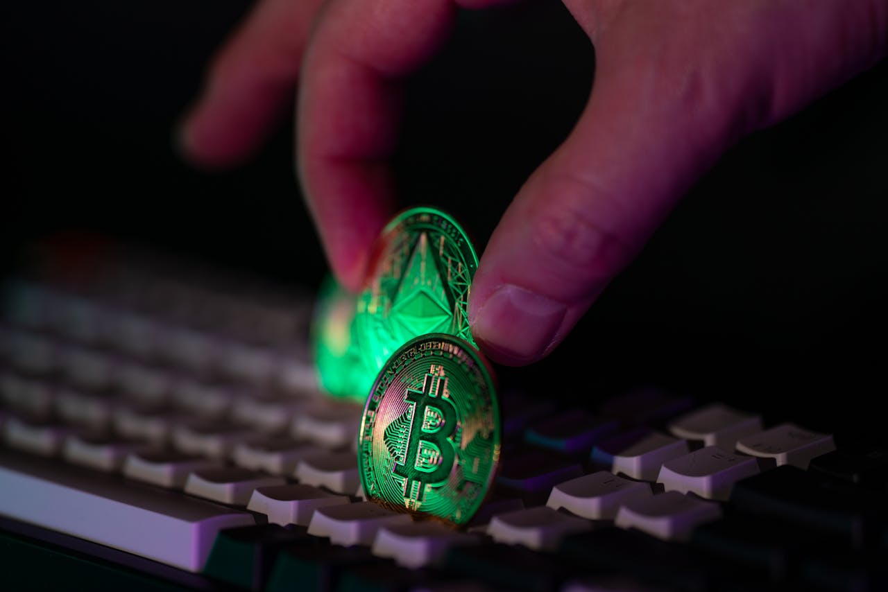 Close-up of a hand placing bitcoin and ethereum coins onto a computer keyboard, symbolizing cryptocurrency and digital finance.