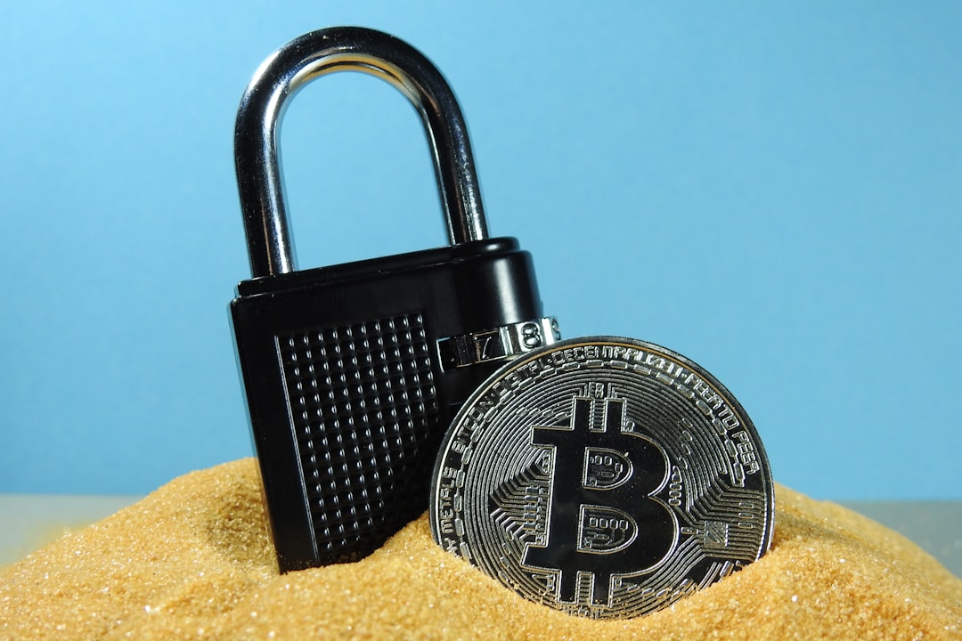 A bitcoin cryptocurrency coin in sand with a black locked padlock